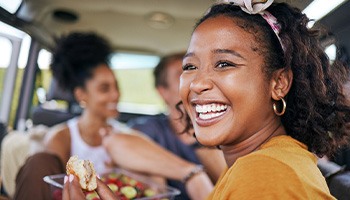Woman smiling while enjoying meal in car with friends