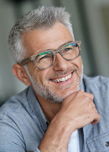 An older gentleman wearing glasses and smiling after receiving his dental implants
