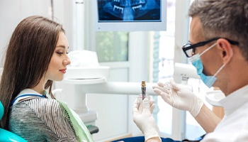 A dentist shows a female patient what a dental implant looks like and explains how it works