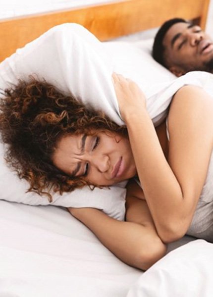 Woman covering her ears while her husband snores