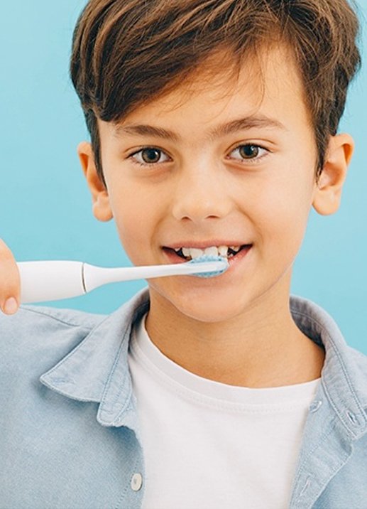 Young boy in white shirt holding his electric toothbrush