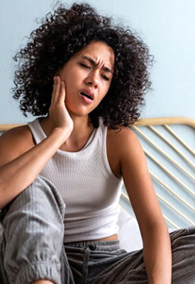 Woman sitting up in bed and rubbing her jaw