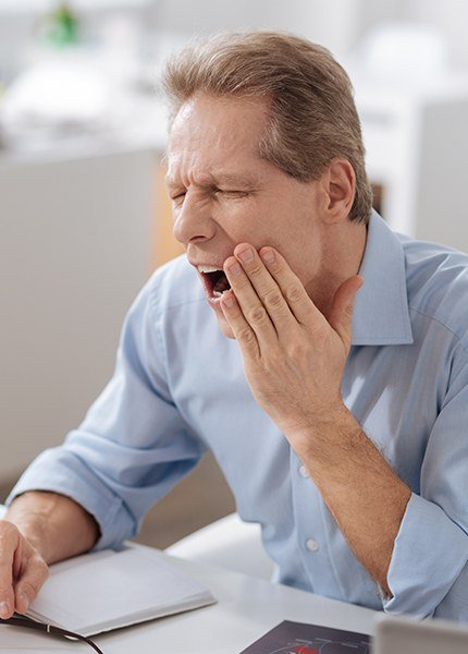 Man in need of T M J therapy holding jaw in pain