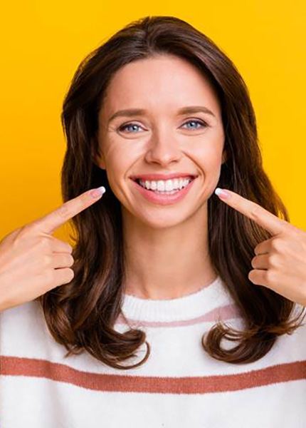 a patient smiling and pointing towards her teeth