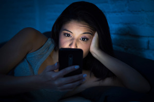 Woman lying in bed looking at her cell phone