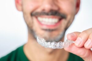 Man smiling while holding up a Sure Smile aligner
